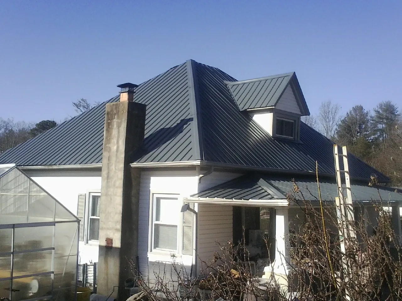 Dark blue standing seam metal roof on a white farmhouse with dormer — Slate & Tile Roof Repair by Roofing Brothers in Braggs