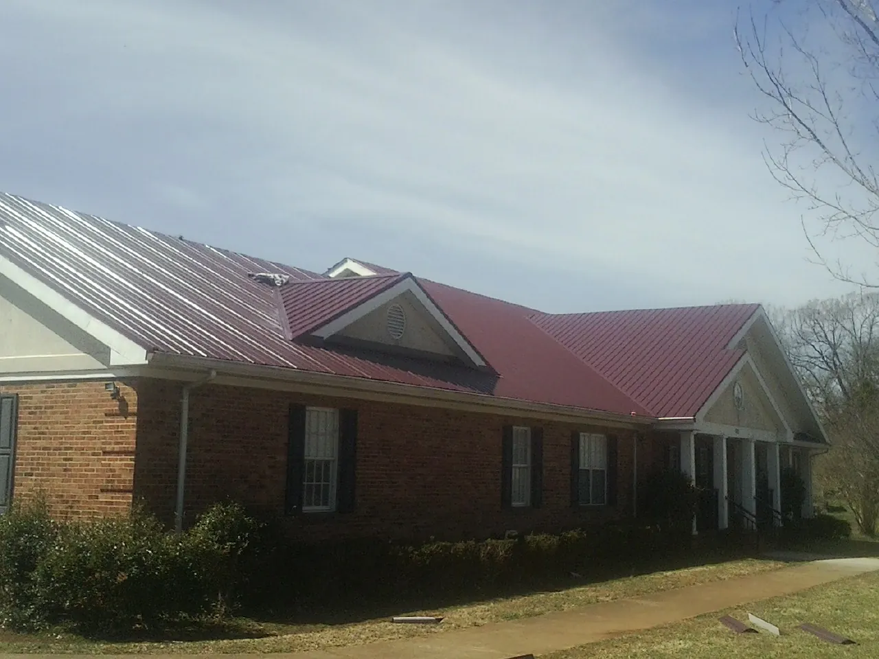 Red metal roof with gabled entries on a long brick building, from a Hail Damage Roof Repair job in Braggs