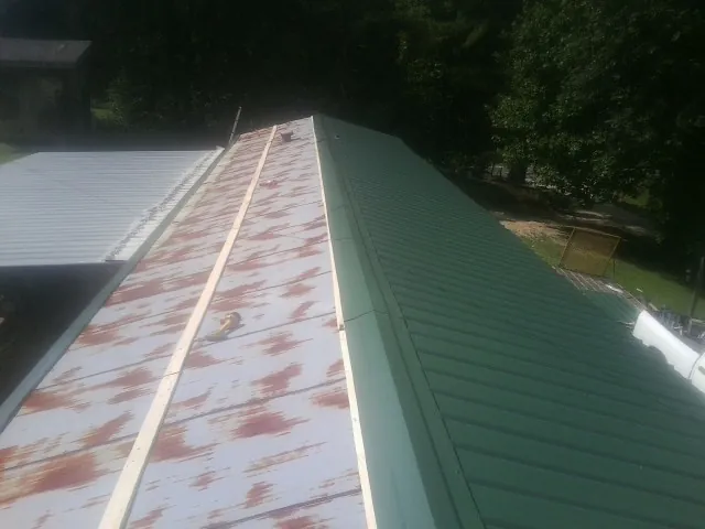 Old rusted panels beside newly installed green metal roofing — Wind Damage Roof Repair by Roofing Brothers in Braggs