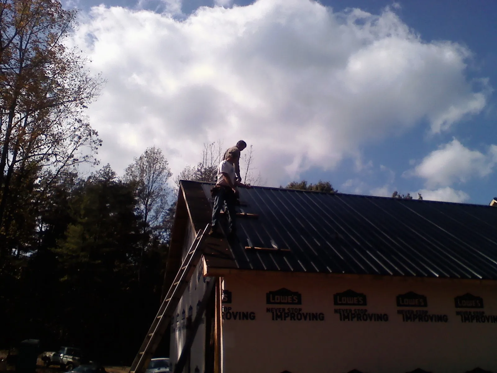 Roofer fastening dark metal panels high against a cloudy sky, from a Roof Inspection job in Braggs