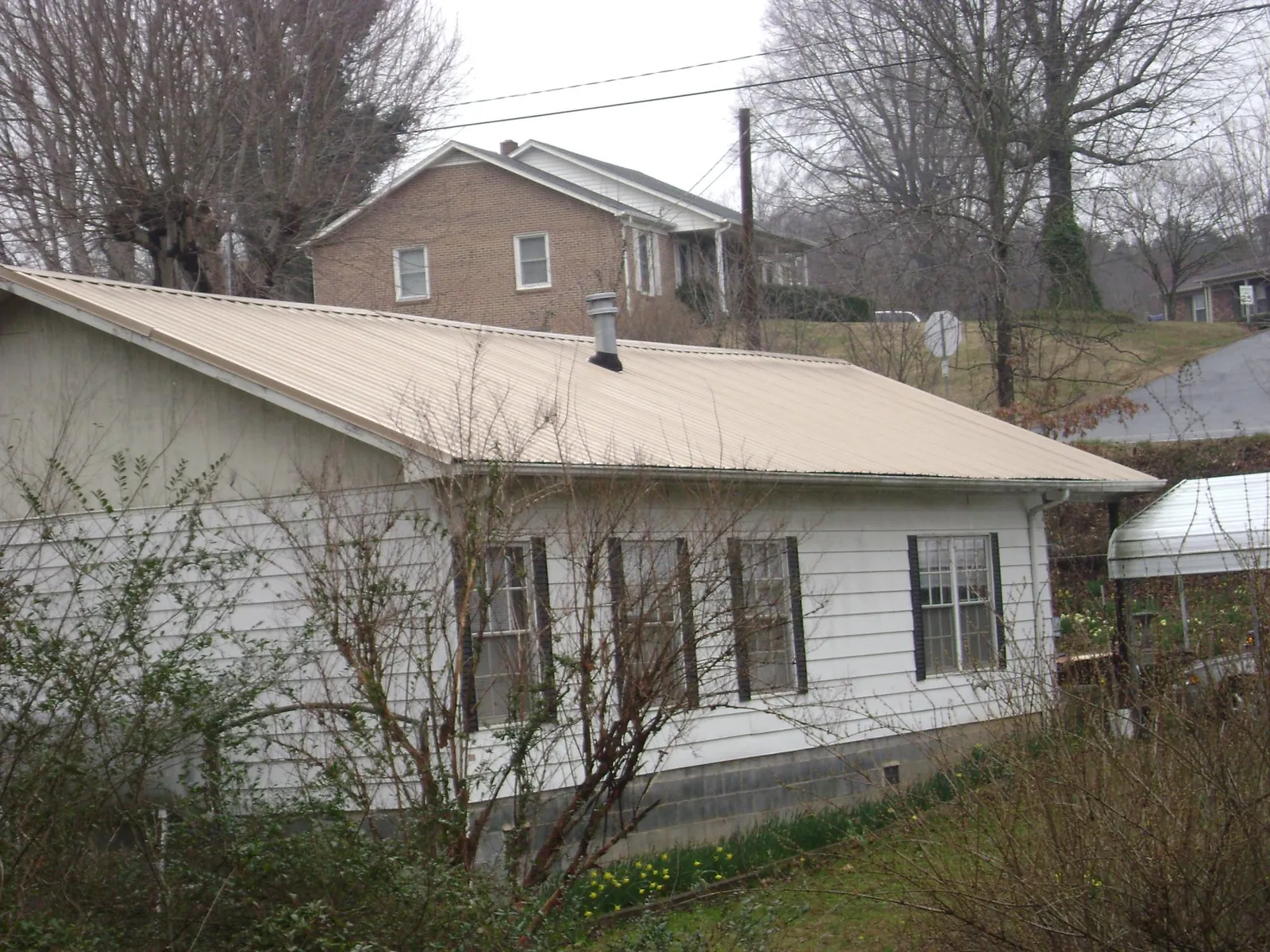 Tan metal roof on a white sided house set into a hillside — Commercial Roofing by Roofing Brothers in Braggs