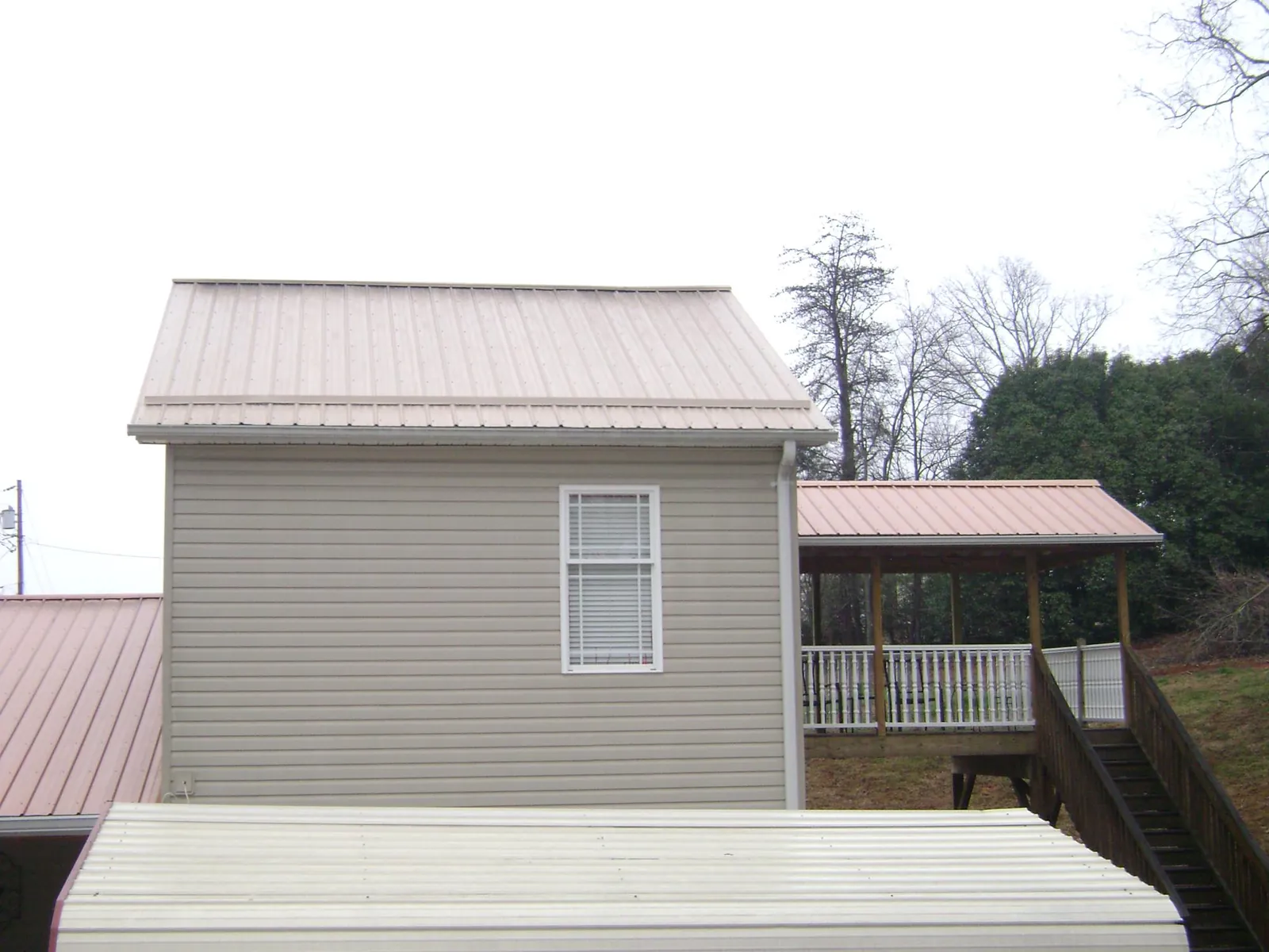 Tan metal roofs on a two story addition and attached porch, from a Roof Replacement job in Braggs